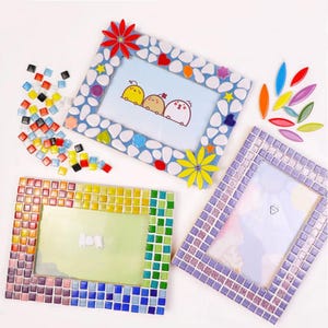 Puede incluir: Tres marcos de fotos decorativos con bordes de mosaico. Un marco tiene un borde azul con detalles de guijarros blancos y adornos florales. Otro marco tiene un borde de mosaico de colores del arcoíris. El tercer marco tiene un borde de mosaico púrpura. Azulejos de mosaico coloridos y detalles decorativos están dispersos alrededor de los marcos.