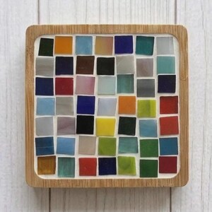 Pode incluir: Um porta-copos quadrado com uma moldura de madeira clara que envolve uma grade de azulejos de mosaico de vidro multicoloridos. As pe&ccedil;as est&atilde;o dispostas num padr&atilde;o de sete por sete, exibindo uma variedade de tons, incluindo vermelho, azul, verde, amarelo e preto.
