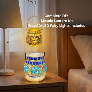 Könnte beinhalten: Komplettes DIY-Mosaik-Laternen-Set mit kostenlosen 20 LED-Feenlichtern. Das Bild zeigt zwei Mosaik-Laternen, eine hängend und eine auf einem Tisch. Die Laternen bestehen aus bunten Glasfliesen und haben einen warmen Schein.