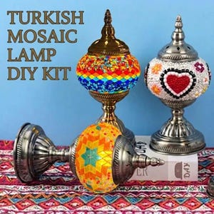 Pode incluir: Três kits de bricolage de candeeiros de mosaico turco com bases de metal e globos de vidro. Um candeeiro apresenta um padrão de diamantes arco-íris, um tem um fundo branco com um coração vermelho e outro um padrão de estrela laranja e turquesa. Texto: TURKISH MOSAIC LAMP DIY KIT.