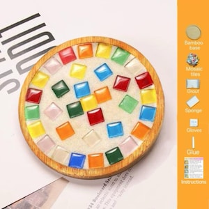 Pode incluir: Um kit de porta-copos redondo de madeira com base de bambu preenchida com argamassa branca e incrustada com azulejos de mosaico de vidro quadrados e coloridos em vermelho, amarelo, verde, azul e laranja. O painel lateral lista os componentes: base de bambu, azulejos de mosaico, argamassa, esponja, luvas, cola e instru&ccedil;&otilde;es.