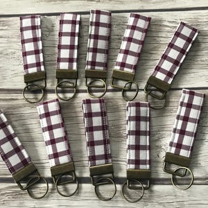 May include: A set of 10 keychains with a white and burgundy gingham pattern. Each keychain has a metal ring and a brown metal clasp.