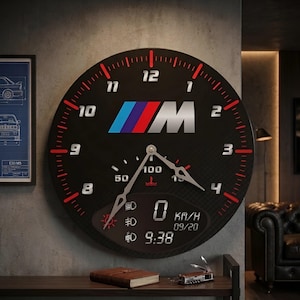 May include: Black wall clock with a car dashboard design, featuring the BMW M logo in blue, red, and silver. Red and white markings indicate the time, with a digital display showing "0 KM/H" and "09/20". The time is 9:38.