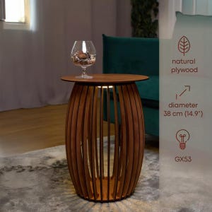 Pode incluir: Uma mesa lateral marrom em forma de barril com um tampo redondo. A mesa é feita de madeira compensada natural e tem ripas de madeira verticais. O diâmetro é de 38 cm. Uma tigela de vidro com itens decorativos fica em cima. A mesa tem uma luz embutida.