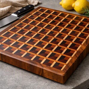 May include: A thick wooden cutting board featuring an intricate end-grain pattern of light, medium, and dark brown wood blocks arranged in a repeating geometric grid. The board has a smooth, polished finish and a rectangular shape with thick edges.