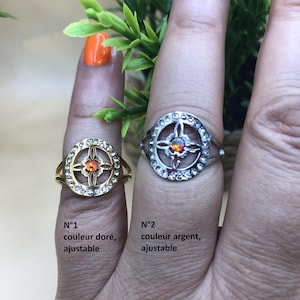 Può includere: Due anelli, uno dorato e uno argentato, ciascuno con una pietra centrale multicolore e circondato da cristalli trasparenti. L'anello dorato è etichettato "N°1 couleur doré, ajustable" e quello argentato "N°2 couleur argent, ajustable".