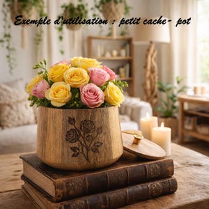 Peut inclure: Un petit pot de fleurs en bois avec un motif de rose, rempli de roses jaunes et roses. Le pot est posé sur deux vieux livres. Le texte "Exemple d'utilisation : petit cache- pot" est visible.