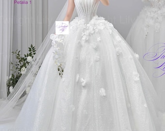 Puede incluir: Vestido de novia blanco sin tirantes con corpiño con cuentas y falda amplia adornada con aplicaciones florales. El vestido incluye un velo largo. Otro vestido está en un maniquí. La imagen se toma en interiores.
