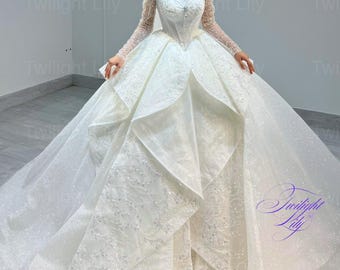 May include: A white wedding dress with a fitted bodice and a full skirt. The dress has a lace overlay and a tulle underskirt. The dress is decorated with sequins and beads. The dress is being worn by a model. The dress is called "Napio 1" and is from the brand "Twilight Lily".