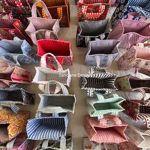 Puede incluir: Una colección de bolsas de tela cuadradas dispuestas en una cuadrícula, con varios patrones coloridos que incluyen rayas, flores y estampados geométricos, con el texto Sandune Design visible en el centro de la imagen.