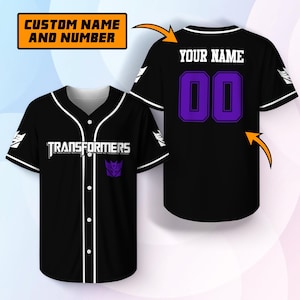 Puede incluir: Una camiseta de béisbol negra con ribetes blancos, la palabra TRANSFORMERS en texto blanco y un logotipo Decepticon morado en la parte delantera. La parte trasera muestra el texto YOUR NAME y el número 00 en morado con bordes negros y blancos.