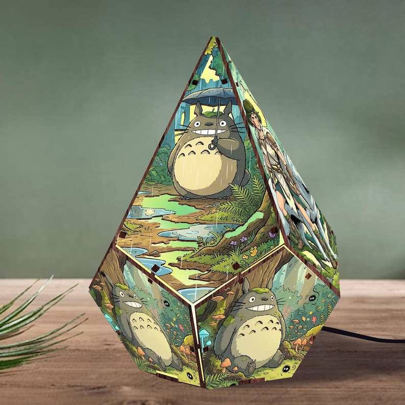 May include: A diamond-shaped wooden lamp featuring colorful illustrations of a large grey creature with a white belly standing in a rainy forest and a lush green woodland scene with small soot sprites and mushrooms on the lower panels.
