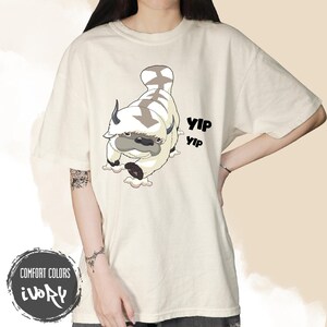 空飛ぶバイソン「イップイップ」をモチーフにしたTシャツ、かわいいファンタジー生物Tシャツ、アニメ風グラフィックシャツ、漫画風ファッション、ユニセックスギフト