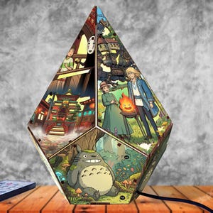 May include: A multi-faceted, diamond-shaped lamp featuring colorful illustrations from animated films. The panels display scenes including a large grey forest creature, a bathhouse, a fire spirit, and a character with a white mask on a bridge.