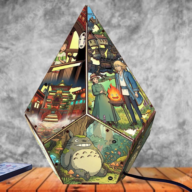 May include: A multi-faceted, diamond-shaped lamp featuring colorful illustrations from animated films. The panels display scenes including a large grey forest creature, a bathhouse, a fire spirit, and a character with a white mask on a bridge.