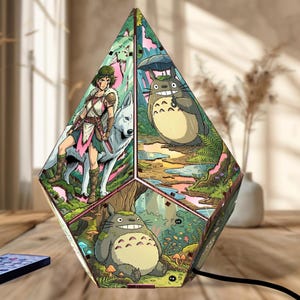 May include: A multi-faceted, diamond-shaped lamp featuring vibrant, colorful illustrations of anime characters. One panel depicts a warrior with a white wolf, another shows a large grey creature with an umbrella, and a third displays a forest scene.