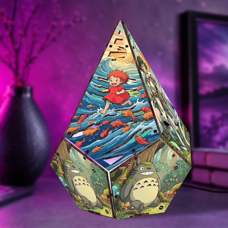 May include: A pyramid-shaped wooden lamp featuring colorful illustrations of animated characters. One side depicts a girl running through ocean waves with orange fish, while another side shows a large grey creature in a forest setting.