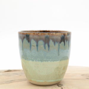 Può includere: Una tazza in ceramica con una glassa verde chiaro e una glassa marrone e blu a goccia.