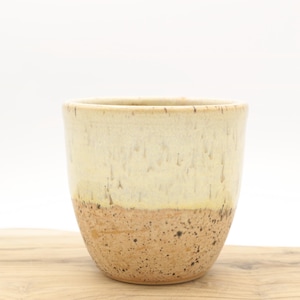 May include: A ceramic planter with a white glaze and a speckled brown base. The planter is a light cream colour with a subtle yellow hue.