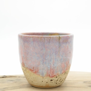 May include: A ceramic cup with a pink, purple and white glaze. The cup has a speckled, textured finish.