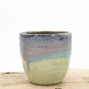 May include: A ceramic cup with a light green glaze and a purple and blue glaze on the top half.