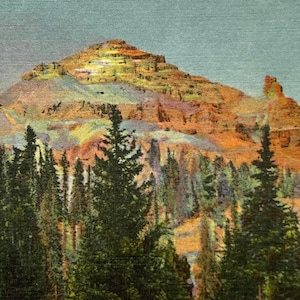 May include: Vintage postcard featuring Beartooth Butte from Beartooth Highway. The image showcases a colorful mountain with layers of orange, yellow, and brown hues, set against a blue sky. Evergreen trees frame the base of the mountain.
