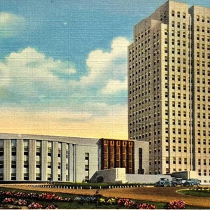 May include: A vintage postcard depicting the North Dakota State Capitol building in Bismarck, North Dakota. The postcard shows a tall, white building with many windows, and a smaller, white building in the foreground. The sky is blue with white clouds.