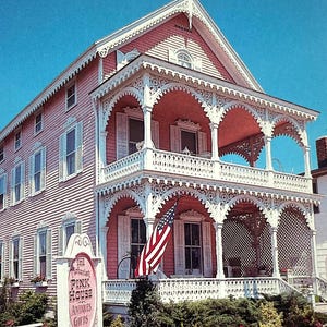 May include: A postcard featuring a pink Victorian house with white trim and a two-story porch. An American flag hangs from the porch. A sign reads "The Pink House Antiques & Gifts". A white picket fence and garden are in front.