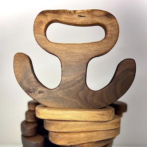 May include: A wooden anchor-shaped coaster with a handle. The coaster is made of dark brown wood and has a natural finish. The coaster is stacked on top of other coasters, creating a tower.
