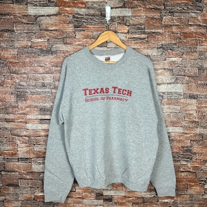 Op de afbeelding: Grijs sweatshirt met de tekst "Texas Tech School of Pharmacy" in rood.