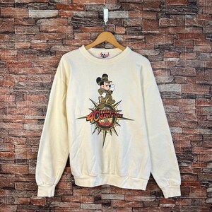 Puede incluir: Una sudadera blanca con un gráfico vintage de Mickey Mouse. El gráfico presenta a Mickey Mouse vestido como explorador con una brújula y el texto "40 Years of Adventure".