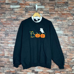 May include: Black Halloween sweatshirt with a white collar. The front features the word "Boo" with orange pumpkins and a white ghost. The sweatshirt is hanging on a wooden hanger.