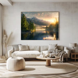 May include: A framed landscape art print depicting a serene lake scene with mountains, trees, and a sunrise. The artwork is displayed above a beige sofa in a living room setting. The room also features a round rug, a coffee table, and a side table.