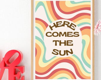 May include: A framed print with a retro design featuring colorful wavy lines in shades of orange, yellow, green, and red. The print has the text "Here Comes The Sun" in a brown font.
