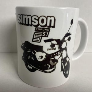Op de afbeelding: Witte keramische mok met een zwart-witte afbeelding van een Simson S51 Enduro motorfiets. De tekst "Simson Enduro S51" is op de mok gedrukt.