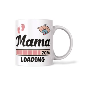 Op de afbeelding: Witte keramische mok met het woord "Mama" in zwart script, roze babyvoetjes en een cartoonbaby met een fopspeen. De mok heeft ook een laadbalkgrafiek en het jaar 2026.