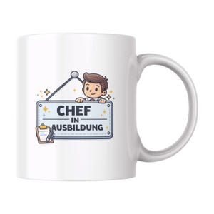 Può includere: Tazza in ceramica bianca con un'illustrazione a cartoni animati di uno chef che tiene in mano un cartello con la scritta "CHEF IN AUSBILDUNG". Il cartello è blu con un bordo bianco e un piccolo blocco note e una penna. La tazza ha un manico curvo.