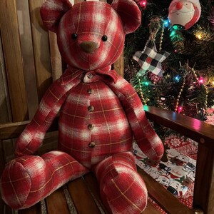 Puede incluir: Un oso de peluche confeccionado con tela de cuadros rojos y blancos. El oso presenta ojos oscuros y redondos, una nariz marr&oacute;n y un cierre frontal decorado con cuatro peque&ntilde;os botones de madera. Tiene un detalle de cuello a juego.