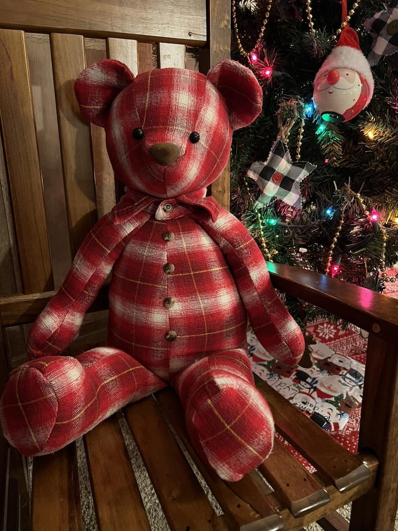 Puede incluir: Un oso de peluche confeccionado con tela de cuadros rojos y blancos. El oso presenta ojos oscuros y redondos, una nariz marr&oacute;n y un cierre frontal decorado con cuatro peque&ntilde;os botones de madera. Tiene un detalle de cuello a juego.