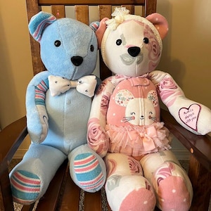 Puede incluir: Dos osos de recuerdo hechos a mano con tela. El oso de la izquierda es azul claro con una pajarita blanca. El oso de la derecha presenta un estampado floral rosa, un peque&ntilde;o tut&uacute;, una diadema blanca y un parche de coraz&oacute;n con el texto 'Mom is always with you'.
