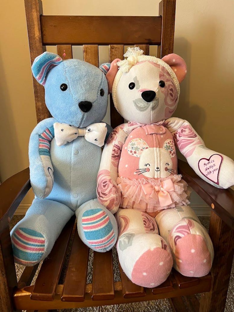 Puede incluir: Dos osos de recuerdo hechos a mano con tela. El oso de la izquierda es azul claro con una pajarita blanca. El oso de la derecha presenta un estampado floral rosa, un peque&ntilde;o tut&uacute;, una diadema blanca y un parche de coraz&oacute;n con el texto 'Mom is always with you'.