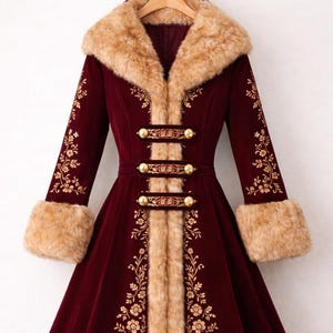 May include: A deep burgundy coat featuring long sleeves, a wide tan faux fur collar, cuffs, and hem. The coat is adorned with gold floral embroidery along the front panels and sleeves, and it fastens with three horizontal tabs with gold buttons.