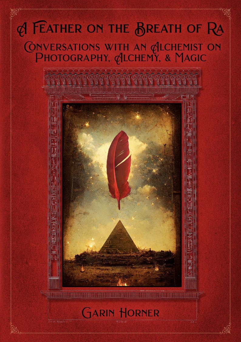 May include: A book cover with a red background and the title "A Feather on the Breath of Ra." The cover features a red feather floating above a pyramid, with text that reads "Conversations with an Alchemist on Photography, Alchemy, & Magic."