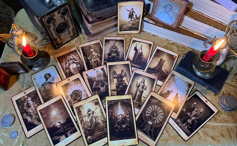 May include: A set of tarot cards with vintage-inspired imagery. The cards feature a variety of scenes and characters, including a woman with a crown, a man with a sword, and a wheel of fortune. The cards are arranged in a circle on a table with candles and other objects.