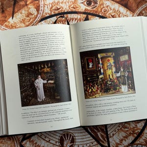 K&ouml;nnte beinhalten: Ein offenes Buch mit zwei Fotografien. Eine zeigt eine Person in einem wei&szlig;en Gewand in einem Raum mit Regalen voller Objekte. Die andere zeigt einen Raum mit Kerzen und einer Person in einem wei&szlig;en Gewand. Das Buch liegt auf einer gemusterten Oberfl&auml;che.
