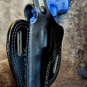 May include: A black leather holster with a blue and black handgun inside. The holster has a snap closure and a belt loop.