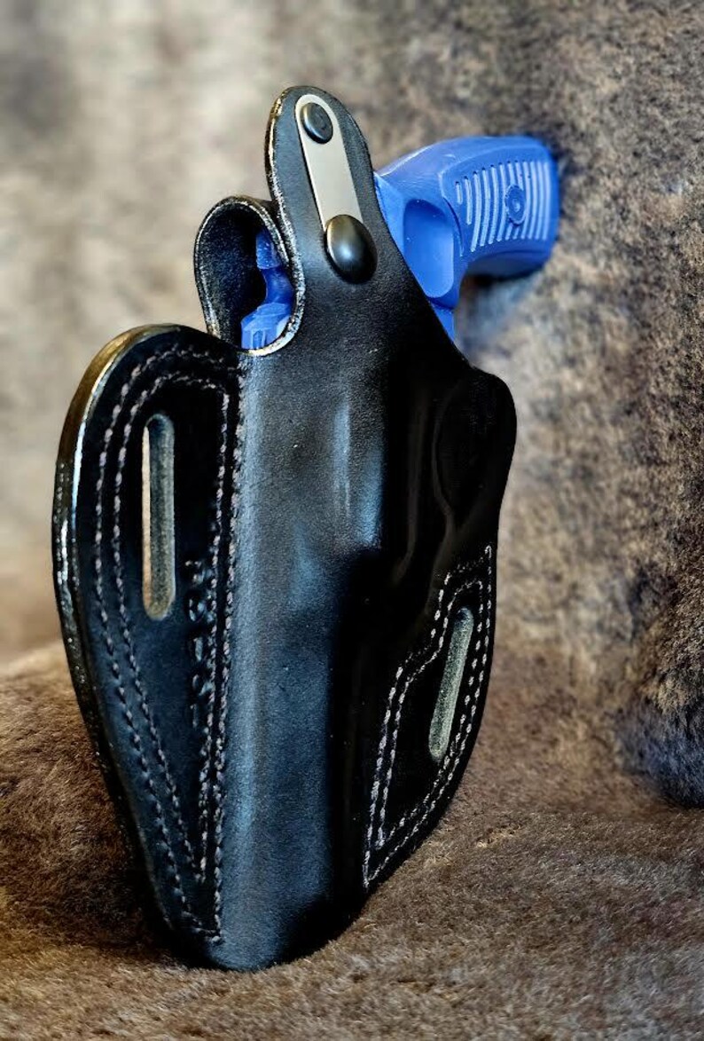 May include: A black leather holster with a blue and black handgun inside. The holster has a snap closure and a belt loop.