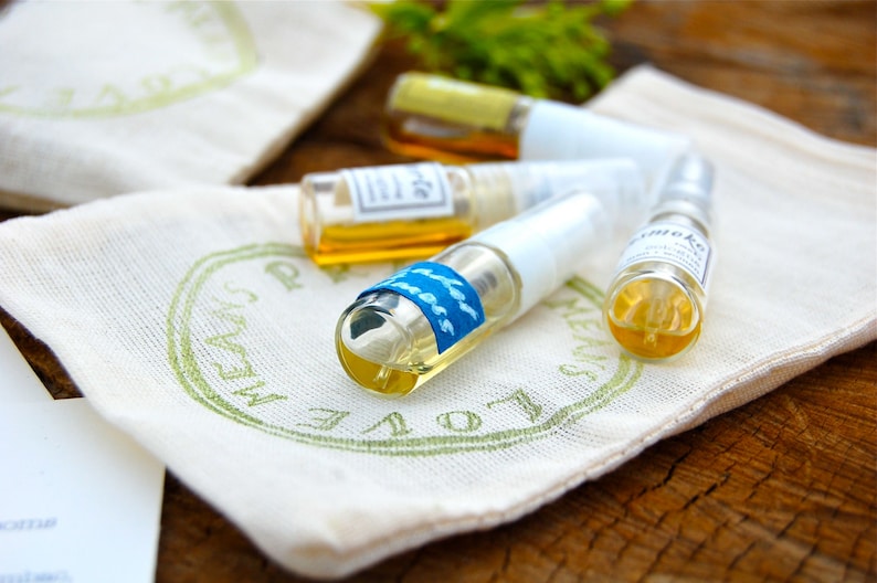 May include: Four small glass bottles with clear liquid and labels, sitting on a white fabric pouch with green lettering that says "LOVE ALWAYS".