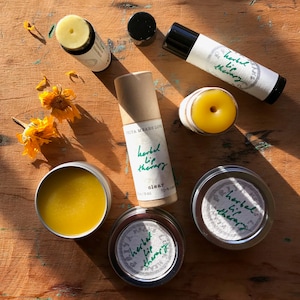 May include: Assortment of lip balm products in various containers, including tubes, tins, and a small jar. The lip balms are labeled "herbal lip therapy" and are in shades of clear, yellow, and brown.
