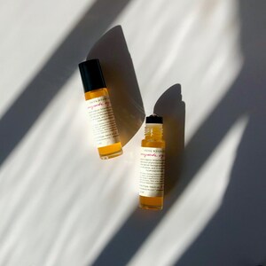 May include: Two small amber glass bottles with rollerball applicators. The bottles are labeled "Priya Meanley - pomegranate eye serum".